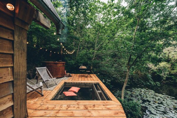 Terrasse de cabane avec transates, une table, jacuzzi et lit de toile dans la forêt.