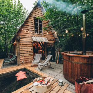 Vu de prêt terrasse de cabane avec transates, une table, jacuzzi, lit de toile et cabane en bois en forêt.